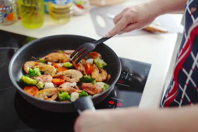 woman-sauteing-shrimps-vegetables-on-pan