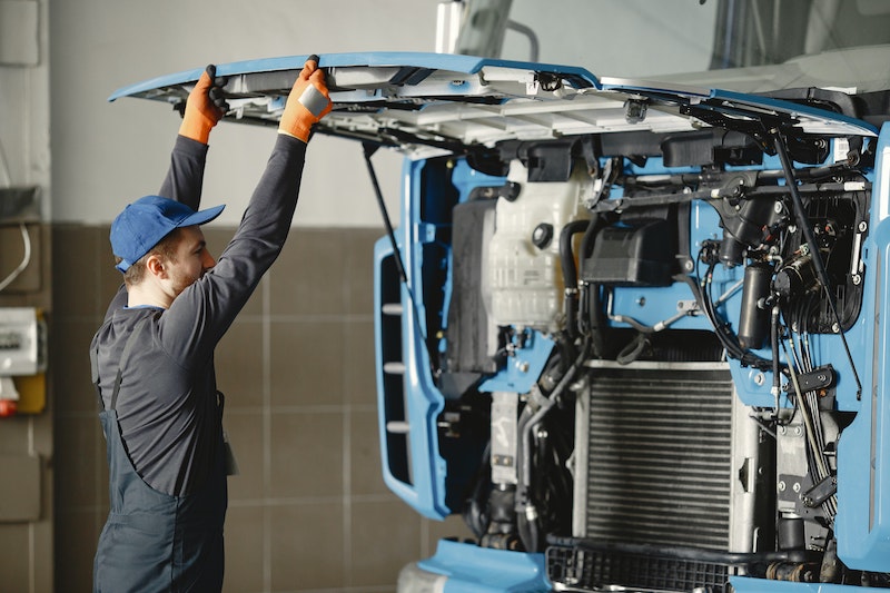 Man in Working Clothes Looking Under Hood of Blue Truck