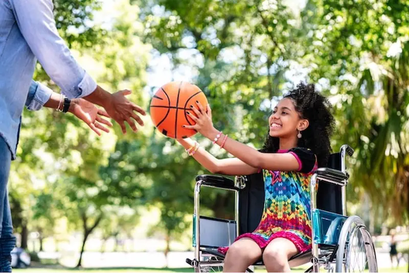 little girl in a wheelchair having fun playing sports basket ball