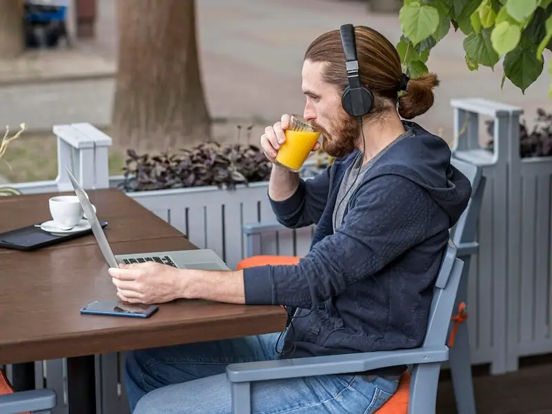 man-enjoying-juice-city-terrace-while-working-laptop