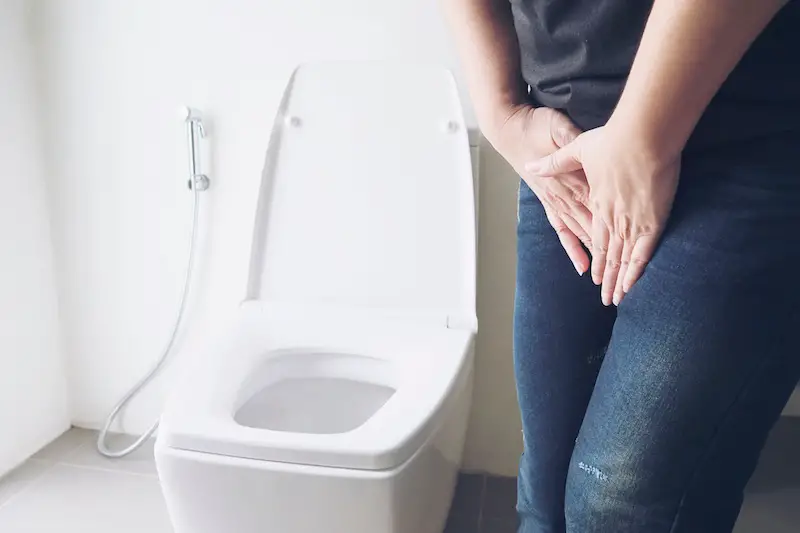 woman-holding-hand-over-pelvic-area-near-toilet-bowl-incontenence-problem
