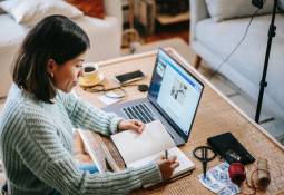 Young woman writing in planner using laptop start side business