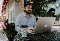 man-smiling-laptop-coffee-outside-american-flag-boost-business-efficiency
