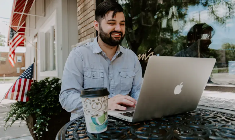 man-smiling-laptop-coffee-outside-american-flag-boost-business-efficiency