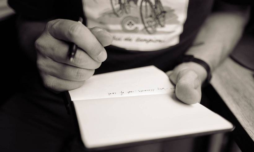 man-holding-pen-writing-on-notepad