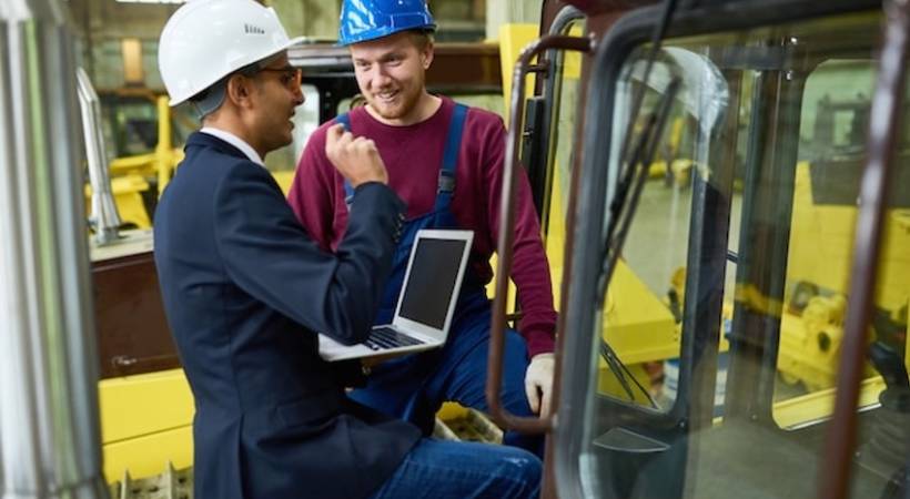 man-in-suit-helmet-laptop-talking-to-forklift-driver.