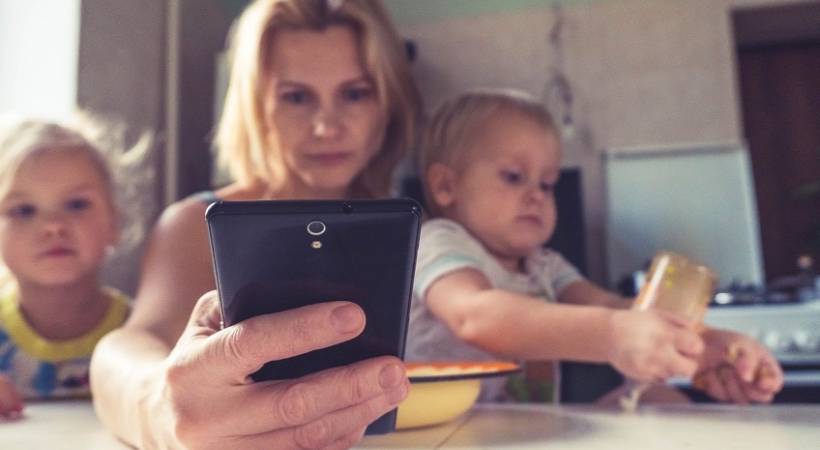 mother-with-todlers-checking-phone-tax-on-mothers-reduced-hours-lower-pay-unemployment