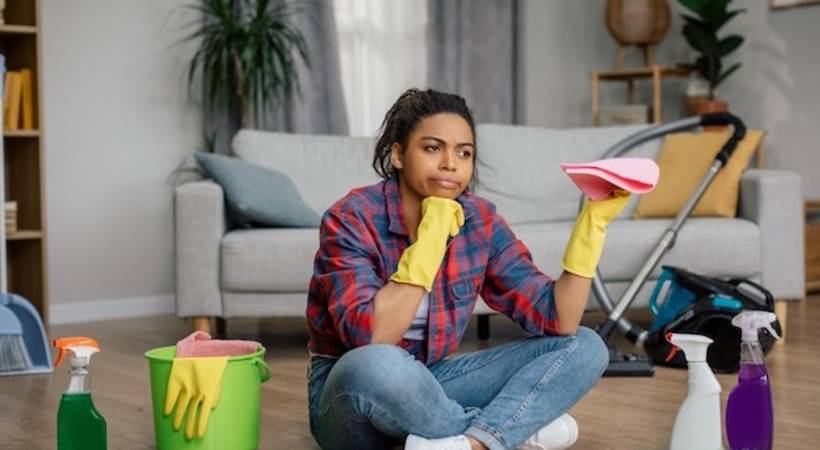 woman in rubber gloves sits on floor with cleaning supplies perplexed expression