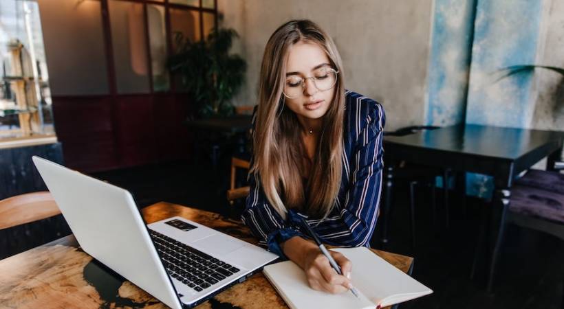 young-woman-writing-her-notebook-blogging-white-laptop-cafe