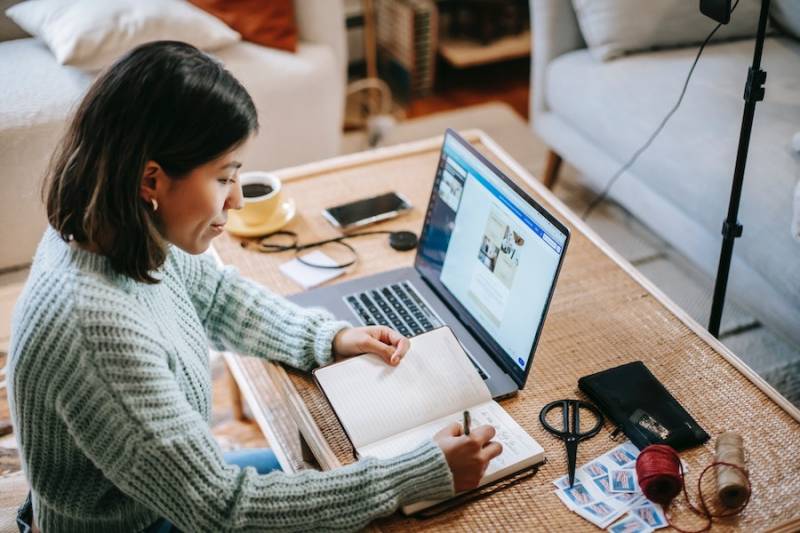 Young woman writing in planner using laptop start side business