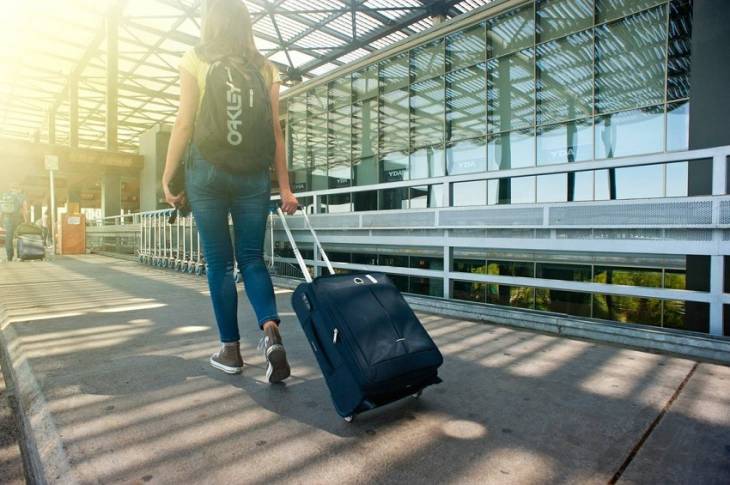 young-woman-backshot-travelling-pulling-suitecase-airport-terminal