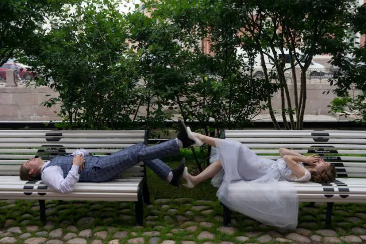 smiling_newlywed_couple_touching_legs_while_lying_on_street_benches