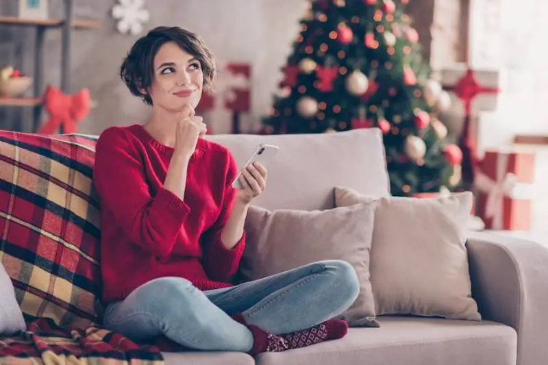 woman-smiling-couch-christmas-tree-using-ai-smartphone - illustration