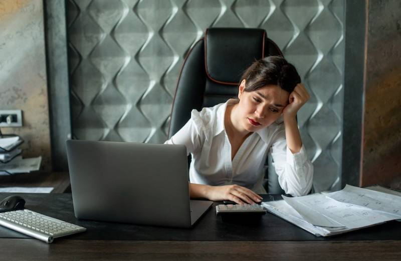 Woman sitting at office desk with documents and laptop computer looking sad stressed worried