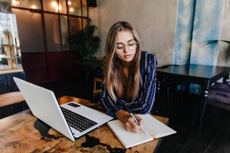 young-woman-writing-her-notebook-blogging-white-laptop-cafe