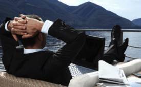 man-suit-relaxing-feet up-ship-deck-laptop-on-deck 