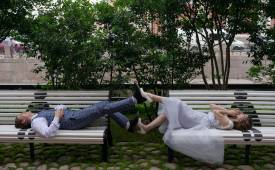 smiling_newlywed_couple_touching_legs_while_lying_on_street_benches