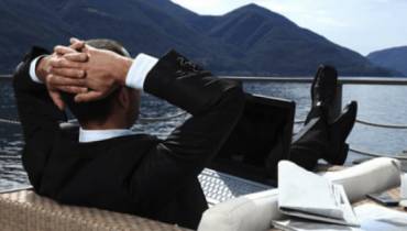 man-suit-relaxing-feet up-ship-deck-laptop-on-deck 