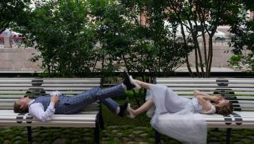 smiling_newlywed_couple_touching_legs_while_lying_on_street_benches