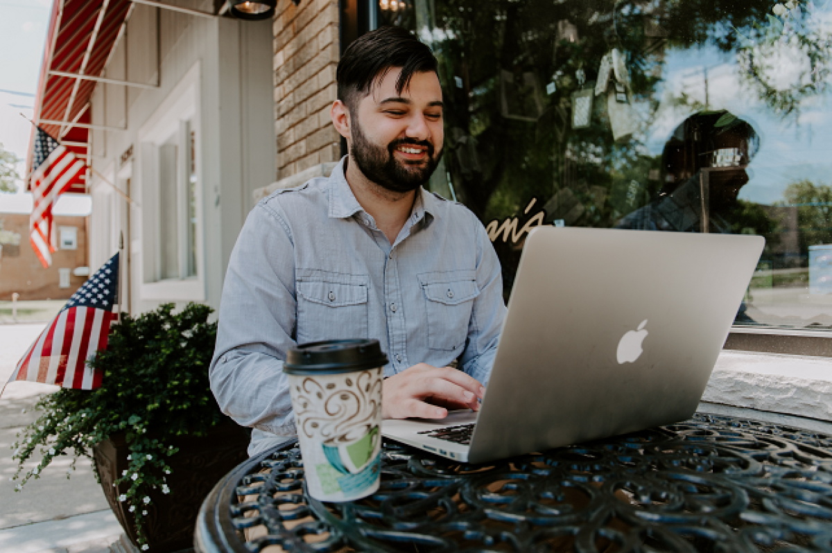 man-smiling-laptop-coffee-outside-american-flag-boost-business-efficiency