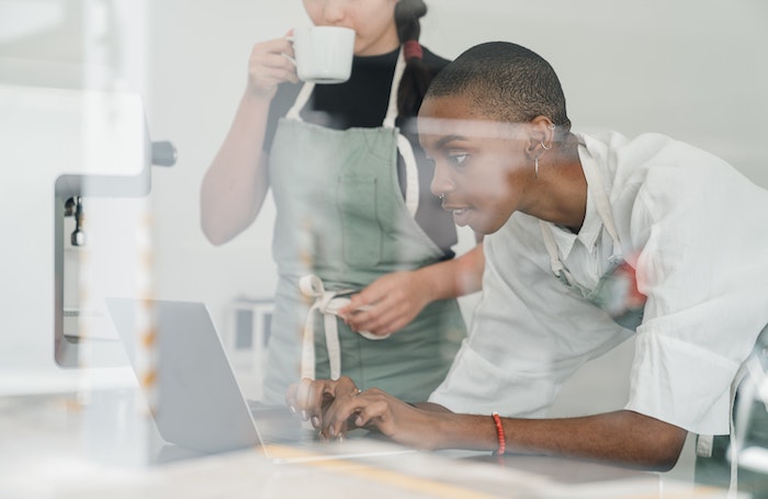 _female_business_owners_with_colleague_using_laptop_at_work.jpg