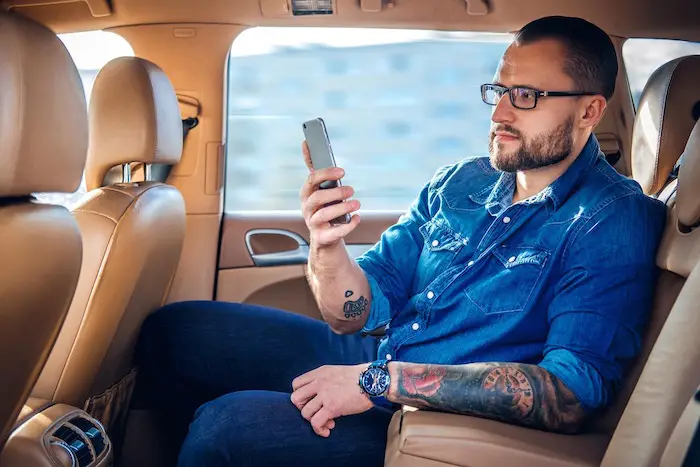 coporate-travel-male-with-tattoo-checking-smart-phone-car.jpg