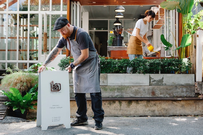 earded_man_installing_business_signboard_while_woman_watering_green_plants