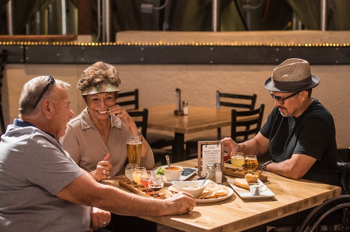 three smiling people sitting beside table with plate of foods and drinks