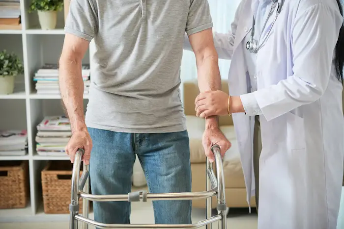female-doctor-helping-male-patient-walk-with-walking-frame