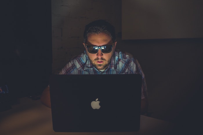 man-wearing-black-sunglasses-dark-room-laptop-online-scam