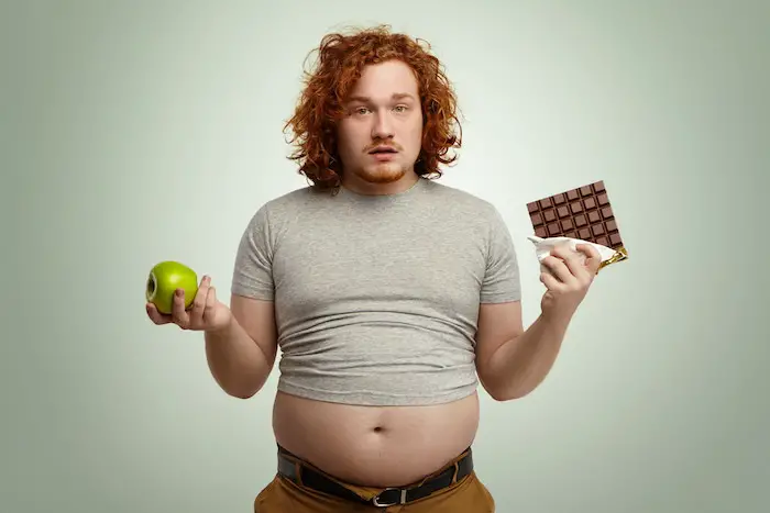 plump-young-man-holding-fresh-apple-bar-chocolate-uncertain-.jpg