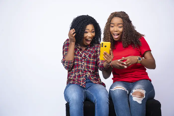 shot-two-young-black-females-looking-phone-together-feeling-excited-surprised