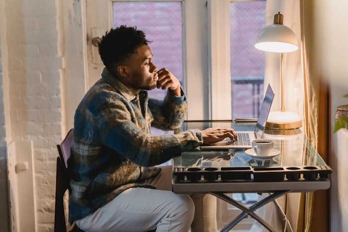 thoughtful_young_black_man_working_distantly_on_laptop_at_home